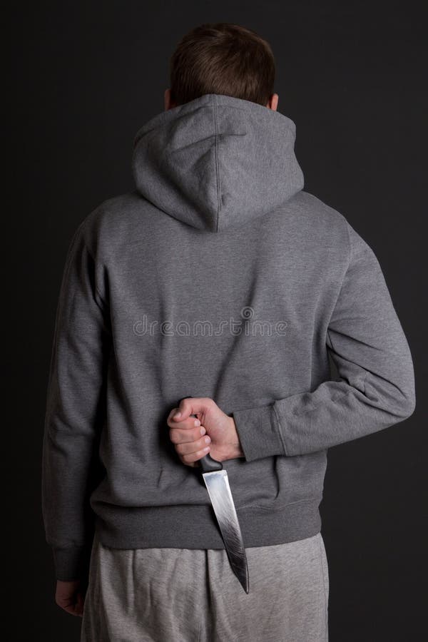 Man hiding knife behind his back over grey background. Man hiding knife behind his back over grey background