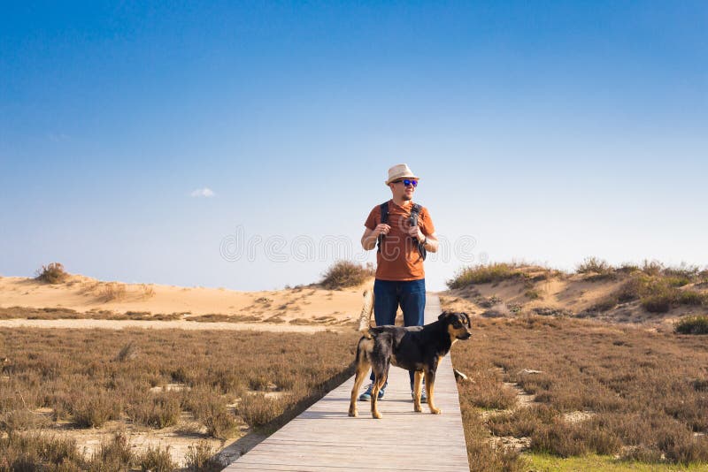 View from behind of a man walking with his dog on a road leading through beautiful landscape. View from behind of a man walking with his dog on a road leading through beautiful landscape.