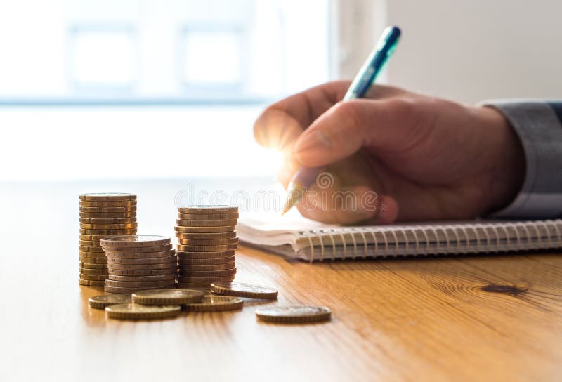 Man counting expenses, budget and savings and writing notes on paper with pen. Budgeting and calculating family living cost. Pension and retirement plan. Stack of coins on table. Man counting expenses, budget and savings and writing notes on paper with pen. Budgeting and calculating family living cost. Pension and retirement plan. Stack of coins on table.