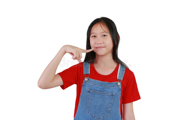 Улыбающаяся азиатская девочка держит пальцы на устах. Ребёнок стоит и смотрит прямо в камеру, изолированную от белой студии стоковая фотография rf