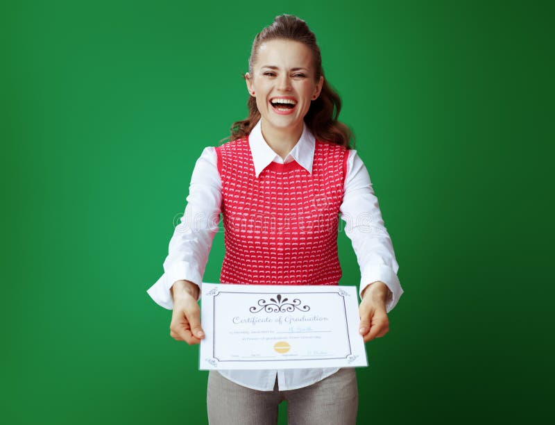 Smiling modern student woman in grey jeans and pink sleeveless shirt showing Certificate of Graduation against green background. Smiling modern student woman in grey jeans and pink sleeveless shirt showing Certificate of Graduation against green background