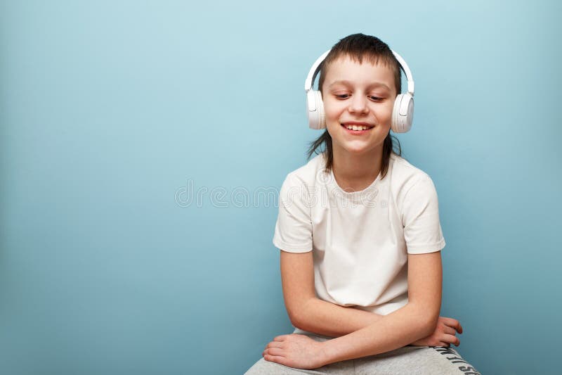 Улыбающийся маленький мальчик слушает музыку в наушниках на изолированном фоне синего цвета в студии стоковое фото rf