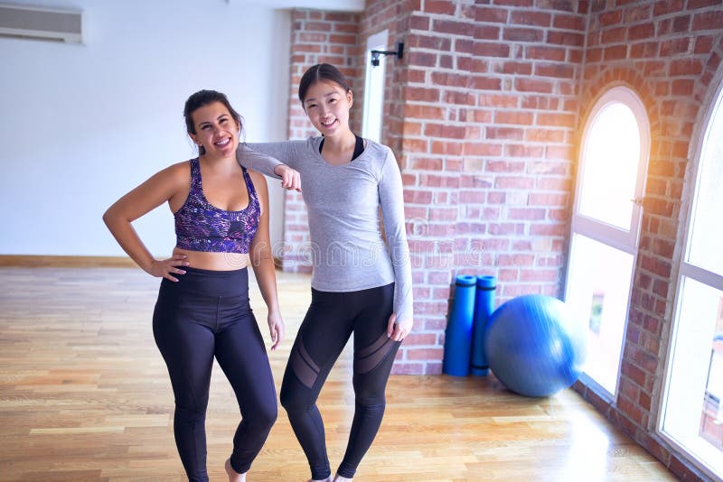 2 young beautiful sportswomen smiling happy. Standing speaking with smile on face after class of yoga at gym. 2 young beautiful sportswomen smiling happy. Standing speaking with smile on face after class of yoga at gym