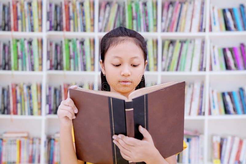 Умная школьница читая книгу в библиотеке стоковые фотографии rf