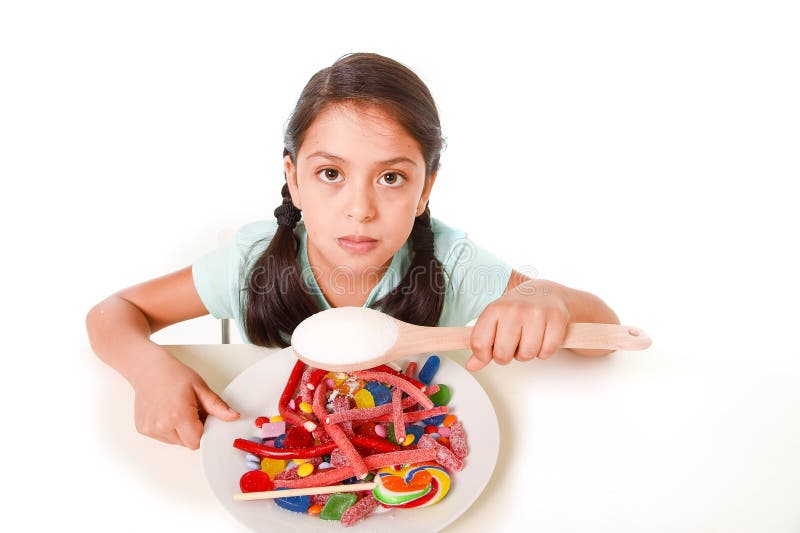 Унылая и уязвимая испанская девочка есть блюдо вполне конфеты и gummies держа ложку сахара в неправильной концепции диеты стоковое изображение rf Унылая и уязвимая испанская девочка есть блюдо вполне конфеты и gummies держа ложку сахара в неправильной концепции диеты стоковое изображение rf
