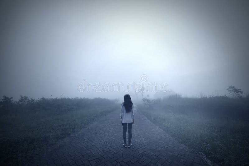 Back view of a sad woman standing alone in a misty morning. Shot in the mountain. Back view of a sad woman standing alone in a misty morning. Shot in the mountain