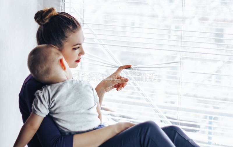 Унылая мать сидя с ее младенцем на windowsill, смотря вне окно и ждать что-то Младенец лежит на ` мамы стоковые изображения Унылая мать сидя с ее младенцем на windowsill, смотря вне окно и ждать что-то Младенец лежит на ` мамы стоковые изображения