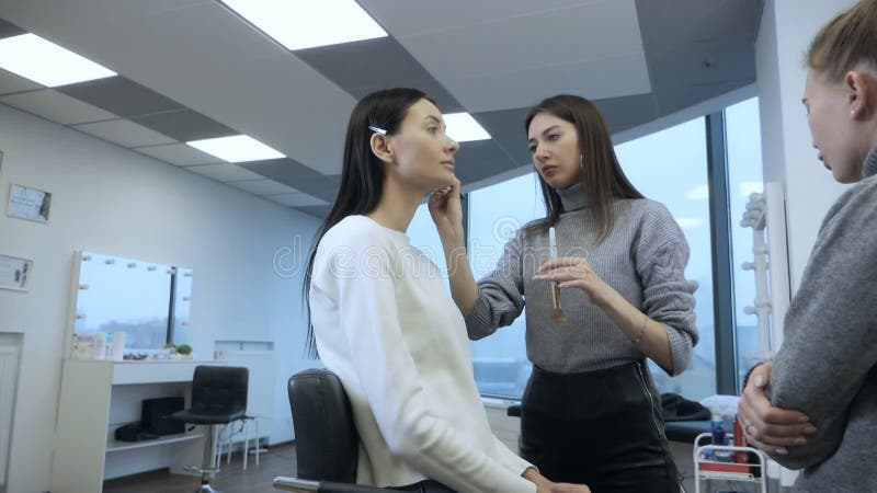 урок макияжа. Студент-макияжист делает макияж для девушки в красивой легкой студии. мастер говорит о видеоматериал
