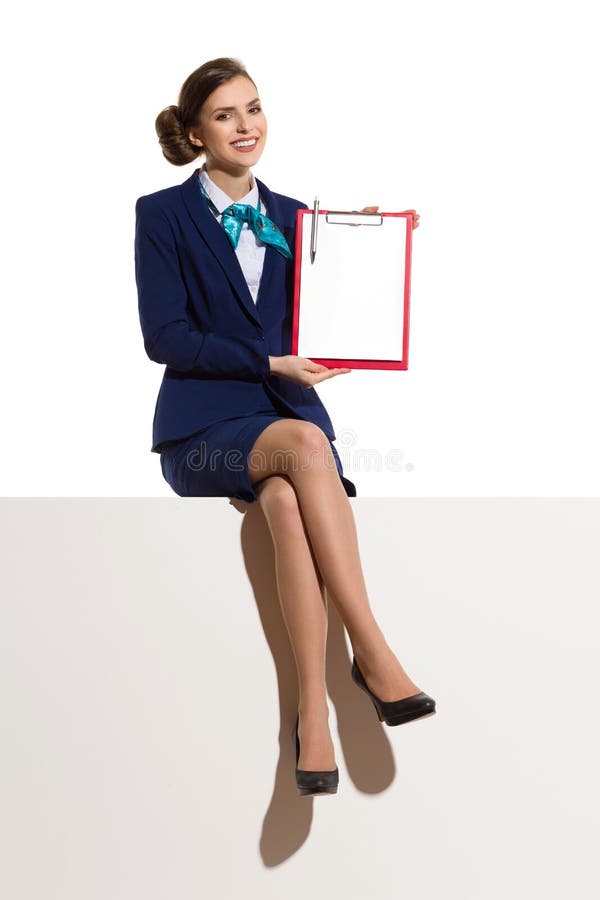 Усмехаясь Stewardess сидя на верхней части и показывать доску сзажимом для бумаги стоковые фотографии rf Усмехаясь Stewardess сидя на верхней части и показывать доску сзажимом для бумаги стоковые фотографии rf