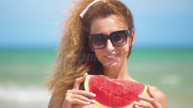 Усмехаясь женщина есть арбуз на пляже Женщина есть вкусный плод лета Счастливое лето видеоматериал