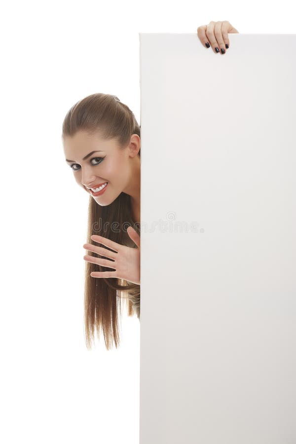 Portrait of smiling enthusiastic pretty woman peeking and waving her hand from behind vertical blank billboard sign over white background. Portrait of smiling enthusiastic pretty woman peeking and waving her hand from behind vertical blank billboard sign over white background.