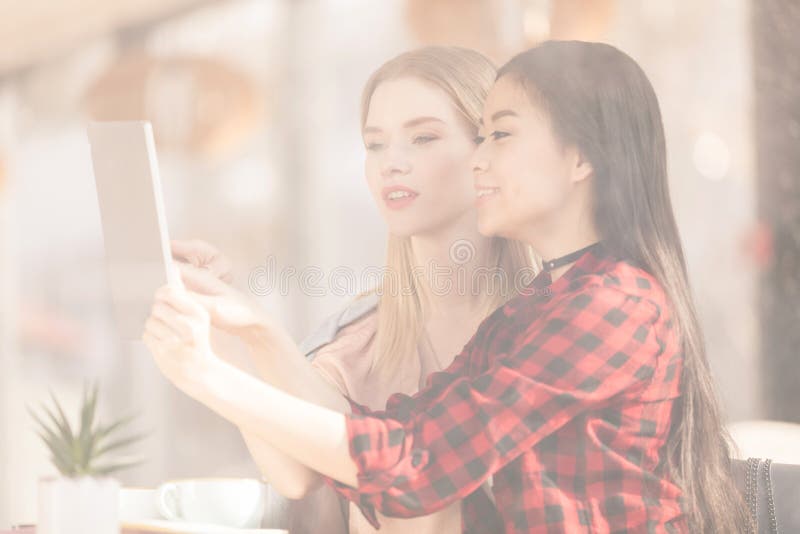 Усмехаясь молодые женщины выпивая кофе и использовать цифровой кофе планшета совместно стоковая фотография Усмехаясь молодые женщины выпивая кофе и использовать цифровой кофе планшета совместно стоковая фотография