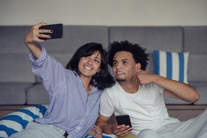 Усмехаясь молодые пары принимая selfies в кровати используя smartphone, они лежат вниз и представлять стоковые фото Усмехаясь молодые пары принимая selfies в кровати используя smartphone, они лежат вниз и представлять стоковые фото