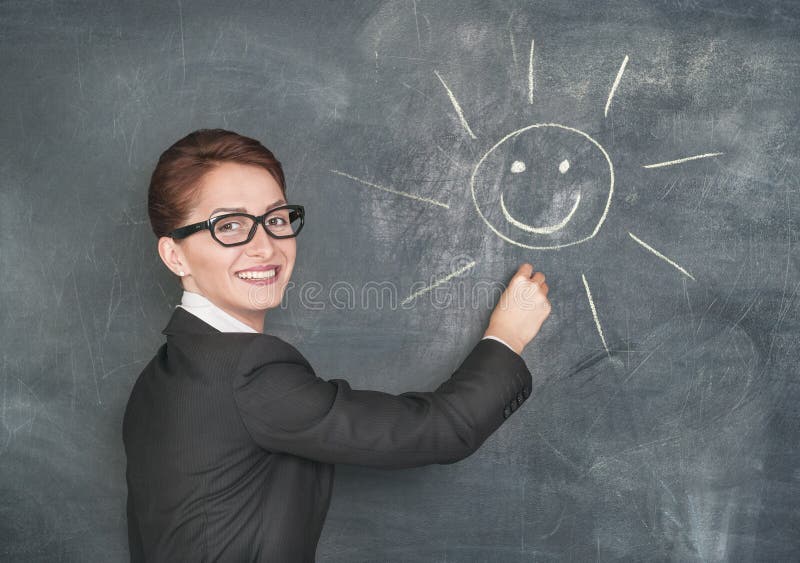 Smiling teacher painting a happy sun on the chalkboard. Smiling teacher painting a happy sun on the chalkboard