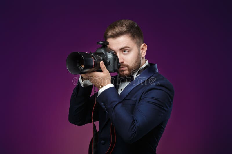Успешный профессиональный фотограф в цифровой фотокамера пользы DSLR смокинга на темной предпосылке стоковое фото rf Успешный профессиональный фотограф в цифровой фотокамера пользы DSLR смокинга на темной предпосылке стоковое фото rf