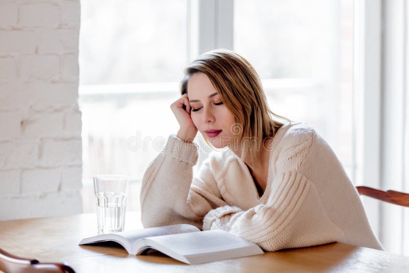 Уставшая девушка в белом свитере с книгой на кухне стоковое изображение Уставшая девушка в белом свитере с книгой на кухне стоковое изображение