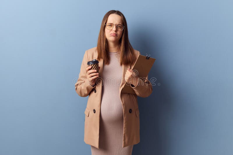 Tired exhausted pregnant woman in beautiful dress and jacket posing  over blue background feeling fatigue of paper work drinking coffee for more energy. Tired exhausted pregnant woman in beautiful dress and jacket posing  over blue background feeling fatigue of paper work drinking coffee for more energy