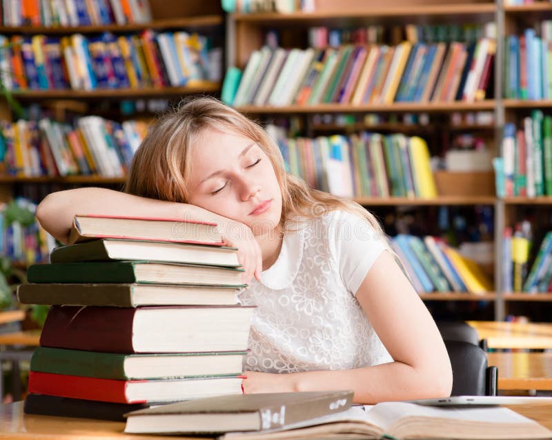 Утомленный студент спит в библиотеке на книгах кучи стоковое фото rf Утомленный студент спит в библиотеке на книгах кучи стоковое фото rf