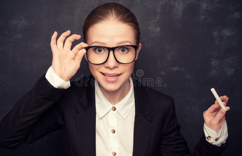 Business woman teacher with glasses and a suit with chalk the lost in thought at a school board. Business woman teacher with glasses and a suit with chalk the lost in thought at a school board