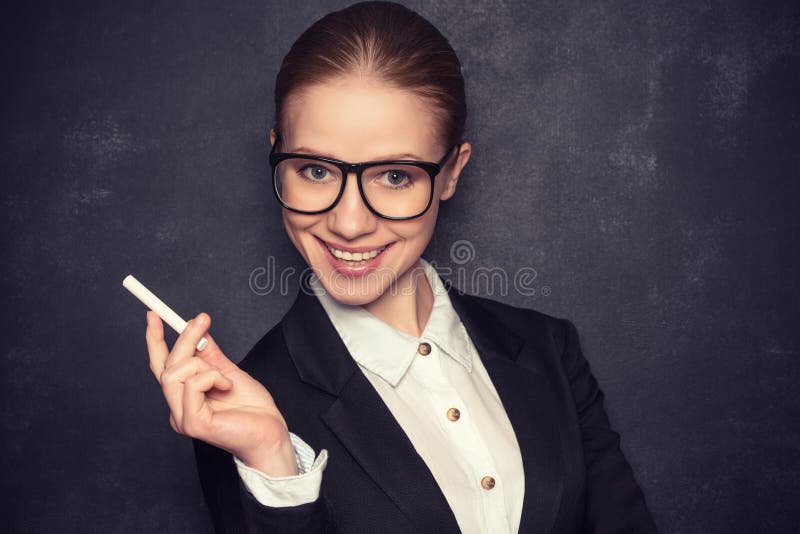 Business woman teacher with glasses and a suit with chalk the lost in thought at a school board. Business woman teacher with glasses and a suit with chalk the lost in thought at a school board