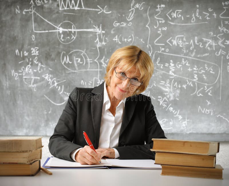 Smiling teacher writing on a register in a classroom. Smiling teacher writing on a register in a classroom