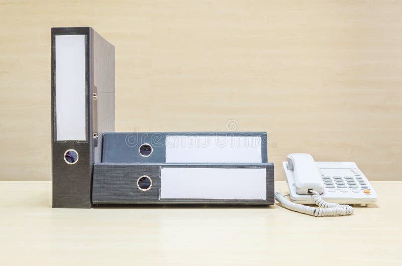 Document file and white phone , office phone on blurred wooden desk and wall textured background in the meeting room under window light. Document file and white phone , office phone on blurred wooden desk and wall textured background in the meeting room under window light