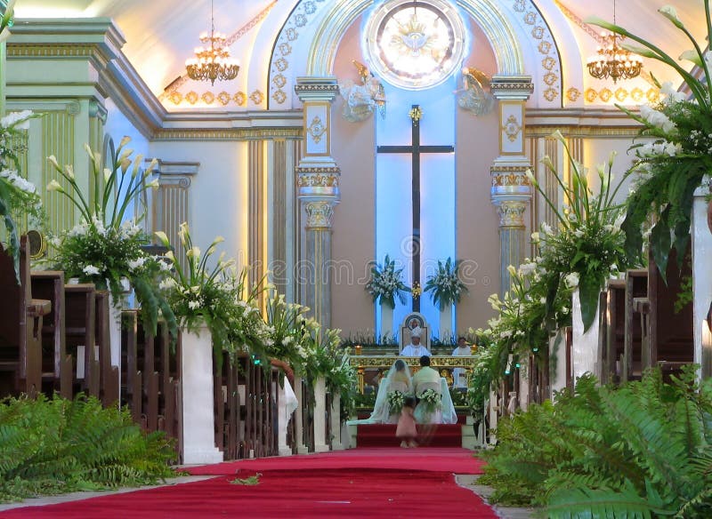 Traditional Filipino Catholic wedding ceremony old style in a cathedral, with flowers arranged along the aisle and the couple at the altar. Dumaguete Cathedral, Negros Oriental, Philippines. Traditional Filipino Catholic wedding ceremony old style in a cathedral, with flowers arranged along the aisle and the couple at the altar. Dumaguete Cathedral, Negros Oriental, Philippines.