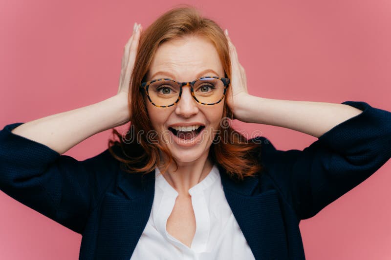 Фото работника офиса положительного redhead женского держит ладони на ушах, смотрит счастливо на камере, носит официальное обмунд стоковая фотография Фото работника офиса положительного redhead женского держит ладони на ушах, смотрит счастливо на камере, носит официальное обмунд стоковая фотография