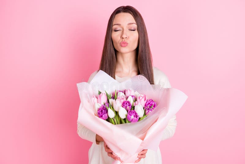 Photo of shiny cute young woman wear white clothes embracing big bunch flowers sending kiss isolated pink color background. Photo of shiny cute young woman wear white clothes embracing big bunch flowers sending kiss isolated pink color background.