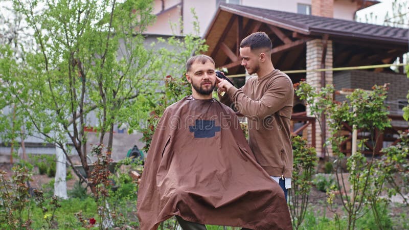 Хорошие ребята, с которыми друзья дома в саду, делая стрижки волос в карантине, используя ножницы акции видеоматериалы