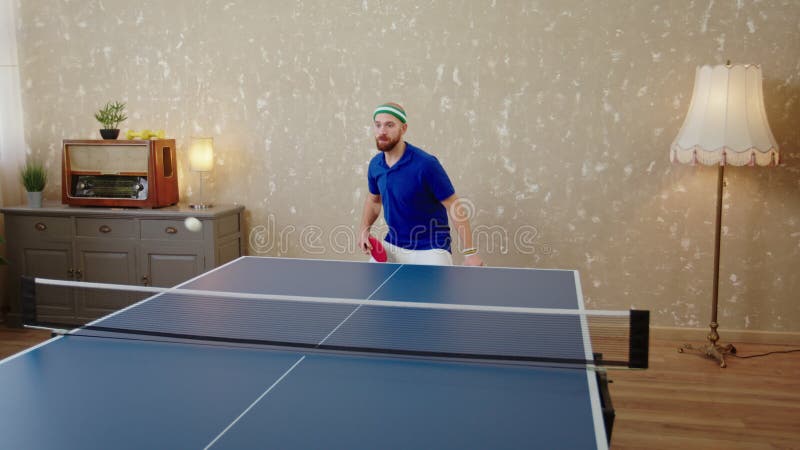 хорошо выглядящий человек, играющий очень концентрированный на пинг-понге или настольном теннисе он бьет по мячу с веслами и акции видеоматериалы