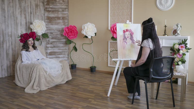Художник рисует портрет от природы Красивая модель, при венок пионов шарлаха на его голове, представляя сидеть в a стоковое фото Художник рисует портрет от природы Красивая модель, при венок пионов шарлаха на его голове, представляя сидеть в a стоковое фото