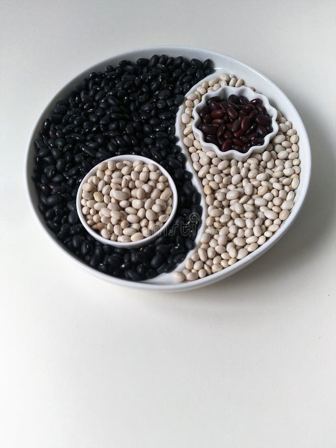 3 цвета фасолей на плите Yin Yang. Черно-белые фасоли лежат в шаре Yin Yang с разделом льют в небольшие круглые блюда и красные и белые фасоли сформированные пятна противоположность, цикл, последовательность взгляд сверху, Flatley, план открытый космос для текста
