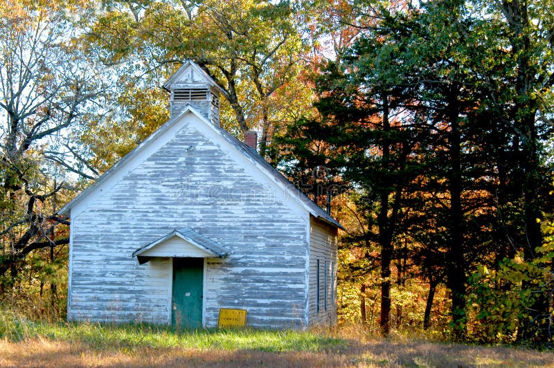 Old church sits on a countryroad in the Mountains of Arkansas. Whitewash is peeling and sign is on the ground. Fall foilage frames in background. Old church sits on a countryroad in the Mountains of Arkansas. Whitewash is peeling and sign is on the ground. Fall foilage frames in background.