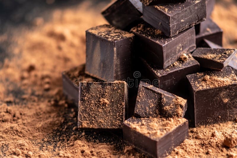 Pieces of dark bitter chocolate with cocoa powder on dark wooden background. The concept of confectionery ingredients. Pieces of dark bitter chocolate with cocoa powder on dark wooden background. The concept of confectionery ingredients