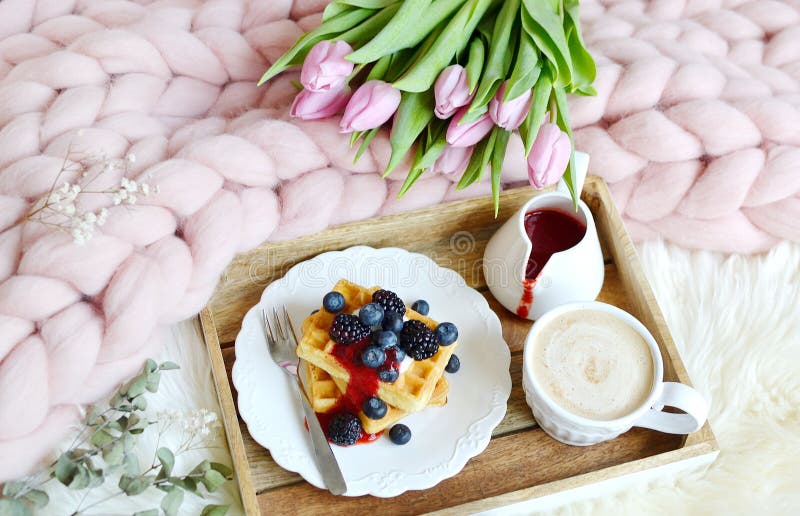 Чашка с капучино и домодельными бельгийскими waffles с соусом клубники и ягодами, розовым пастельным гигантским одеялом стоковое изображение Чашка с капучино и домодельными бельгийскими waffles с соусом клубники и ягодами, розовым пастельным гигантским одеялом стоковое изображение