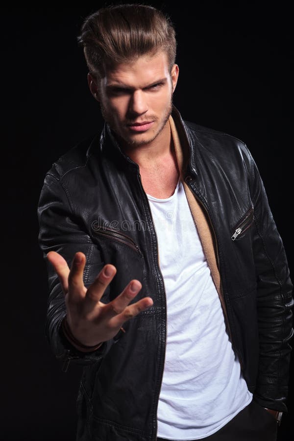 Young fashion man in leather jacket is looking very upset and makes a hand gesture on black background. Young fashion man in leather jacket is looking very upset and makes a hand gesture on black background