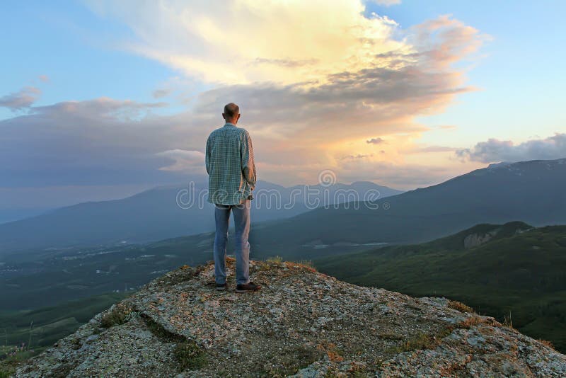 A man stands on top of the evening and looking at the village beneath the mountain. Man sees the approach of change and thunderstorms. human fear of the unknown future. A man stands on top of the evening and looking at the village beneath the mountain. Man sees the approach of change and thunderstorms. human fear of the unknown future.