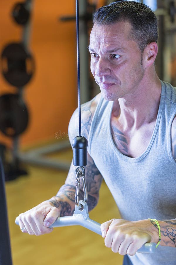 Man making pulley pushdown standing - tricep exercise - at the gym - start exercise - focus on the man face. Man making pulley pushdown standing - tricep exercise - at the gym - start exercise - focus on the man face