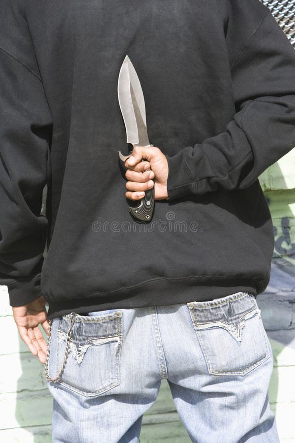 Rear view of a young male holding knife behind back. Rear view of a young male holding knife behind back