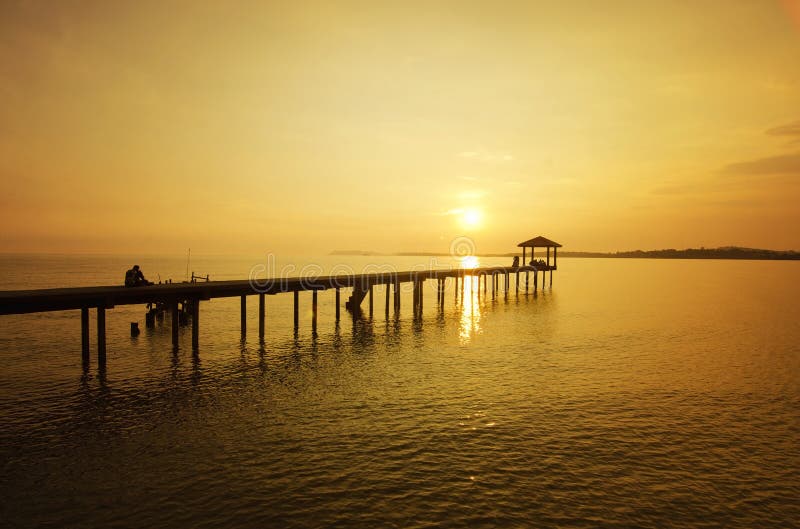 Человек сидя на мосте самостоятельно во время захода солнца