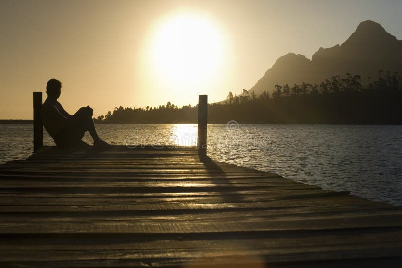 Side view of man sitting on dock by lake enjoying sunset. Side view of man sitting on dock by lake enjoying sunset