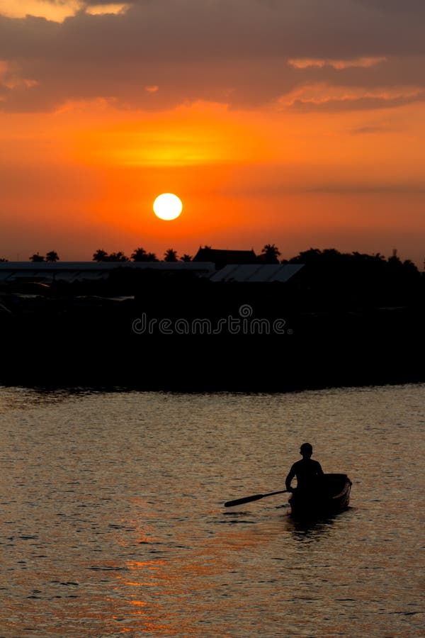 Человек Rowing в шлюпке на заходе солнца стоковое фото Человек Rowing в шлюпке на заходе солнца стоковое фото