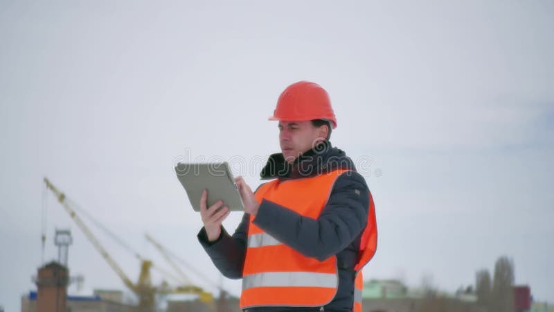 Человек архитектора построителя в шлеме с таблеткой на строительной площадке работник строительной промышленности в зиме строя a