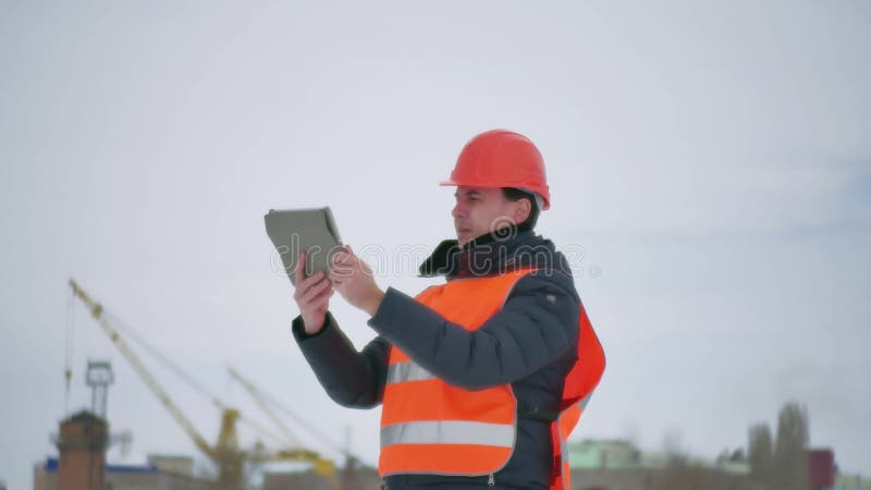 Человек архитектора построителя в шлеме с таблеткой на строительной площадке работник строительной промышленности в зиме строя a