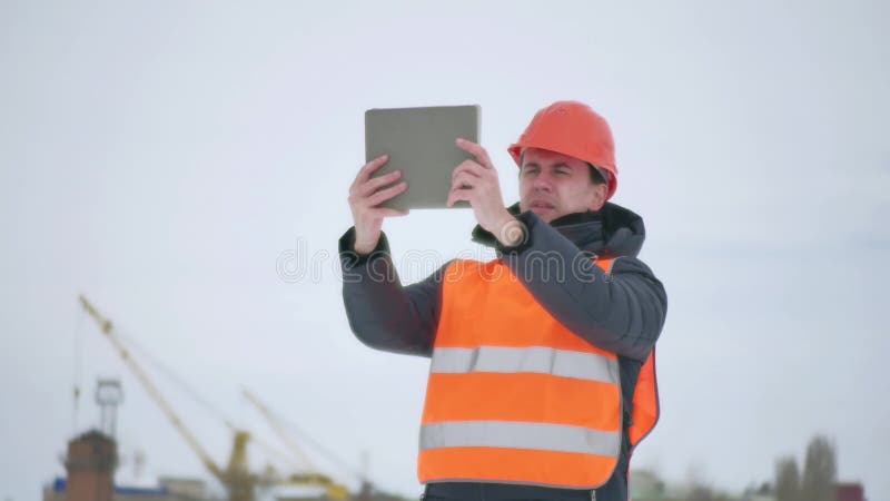 Человек архитектора построителя в шлеме с таблеткой на строительной площадке работник строительной промышленности в зиме строя a