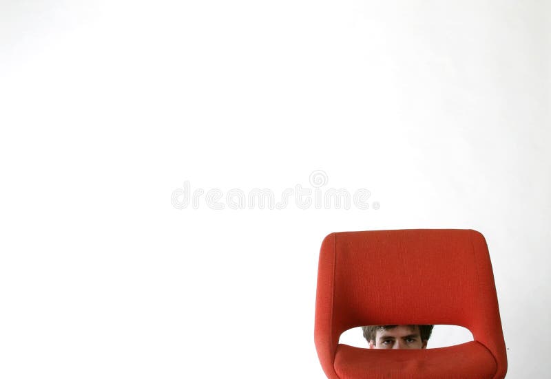 Shy man hiding behind a red chair. Shy man hiding behind a red chair.