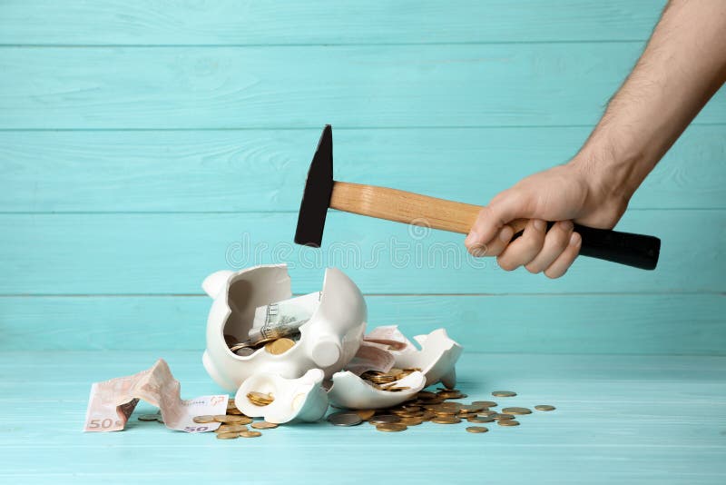 Man breaking piggy bank with hammer on table. Man breaking piggy bank with hammer on table