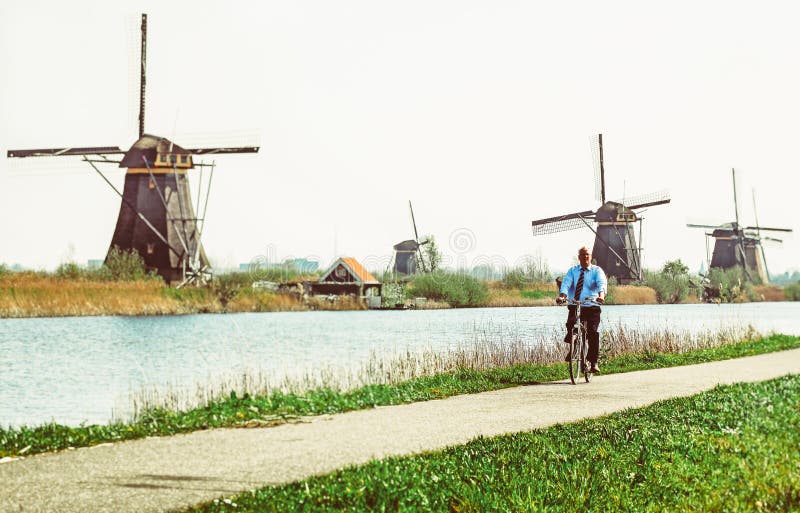 KINDERDIJK, NETHERLANDS - APRIL 1: Senior man on bike and windmills at open air musem at Kinderdijk on April 1, 2014 in Kinderdijk. KINDERDIJK, NETHERLANDS - APRIL 1: Senior man on bike and windmills at open air musem at Kinderdijk on April 1, 2014 in Kinderdijk