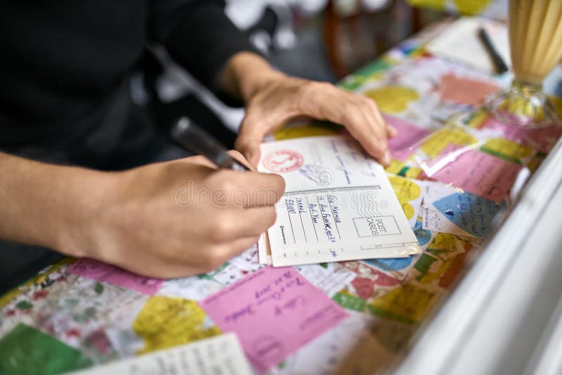 Hanoi, Vietnam - 26 February 2019: man is writing a postcard on a colorful table which pasted with multicolored cards with messages in the cafe. Closeup. Horizontal. Editorial. Hanoi, Vietnam - 26 February 2019: man is writing a postcard on a colorful table which pasted with multicolored cards with messages in the cafe. Closeup. Horizontal. Editorial.